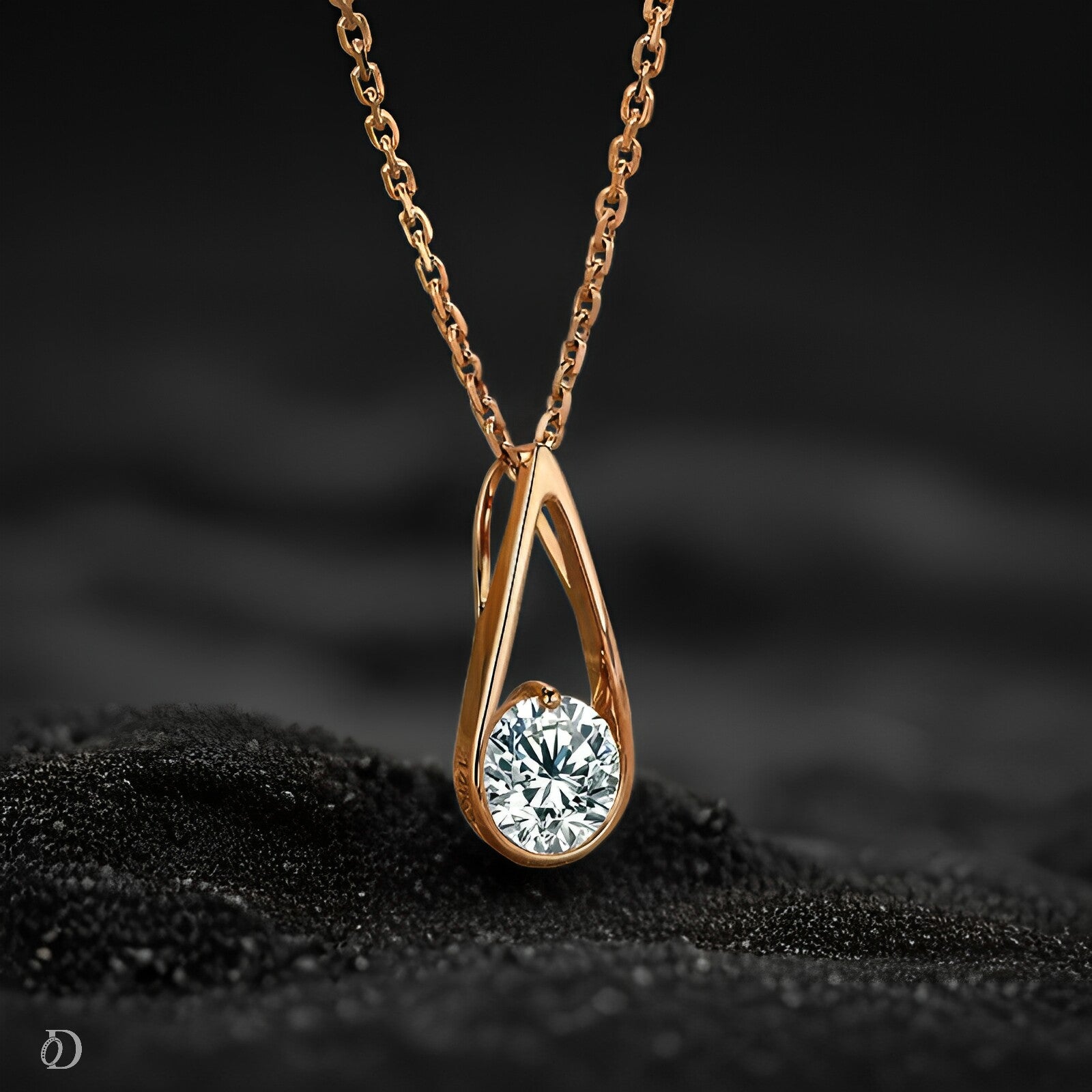Rose gold teardrop-shaped necklace with a diamond on a black textured surface