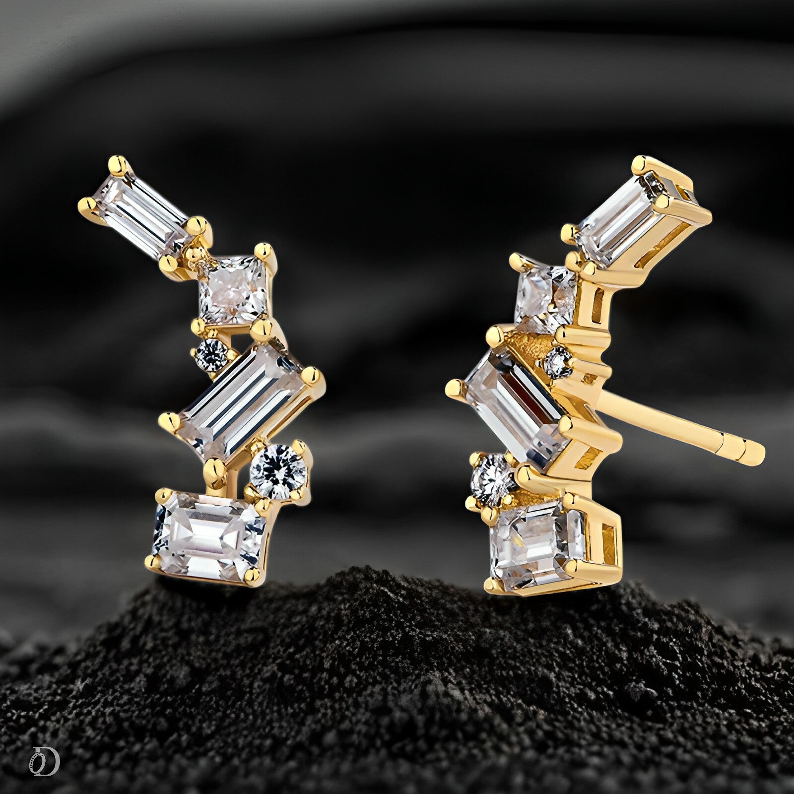 Gold earrings with clear gemstones on a black sand-like surface