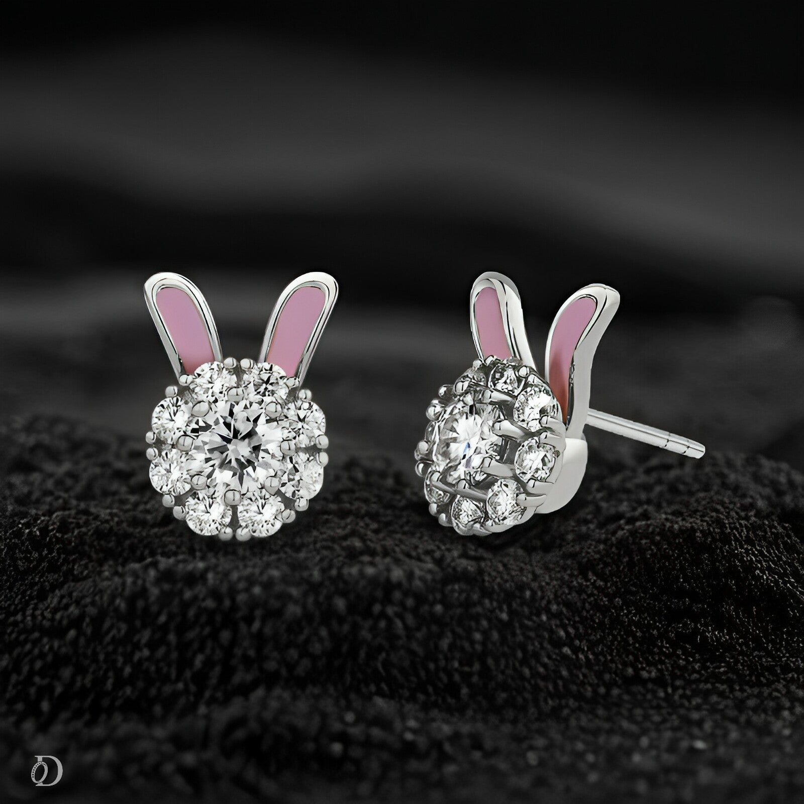 Silver bunny ear-shaped earrings with pink inner ears on a dark textured surface