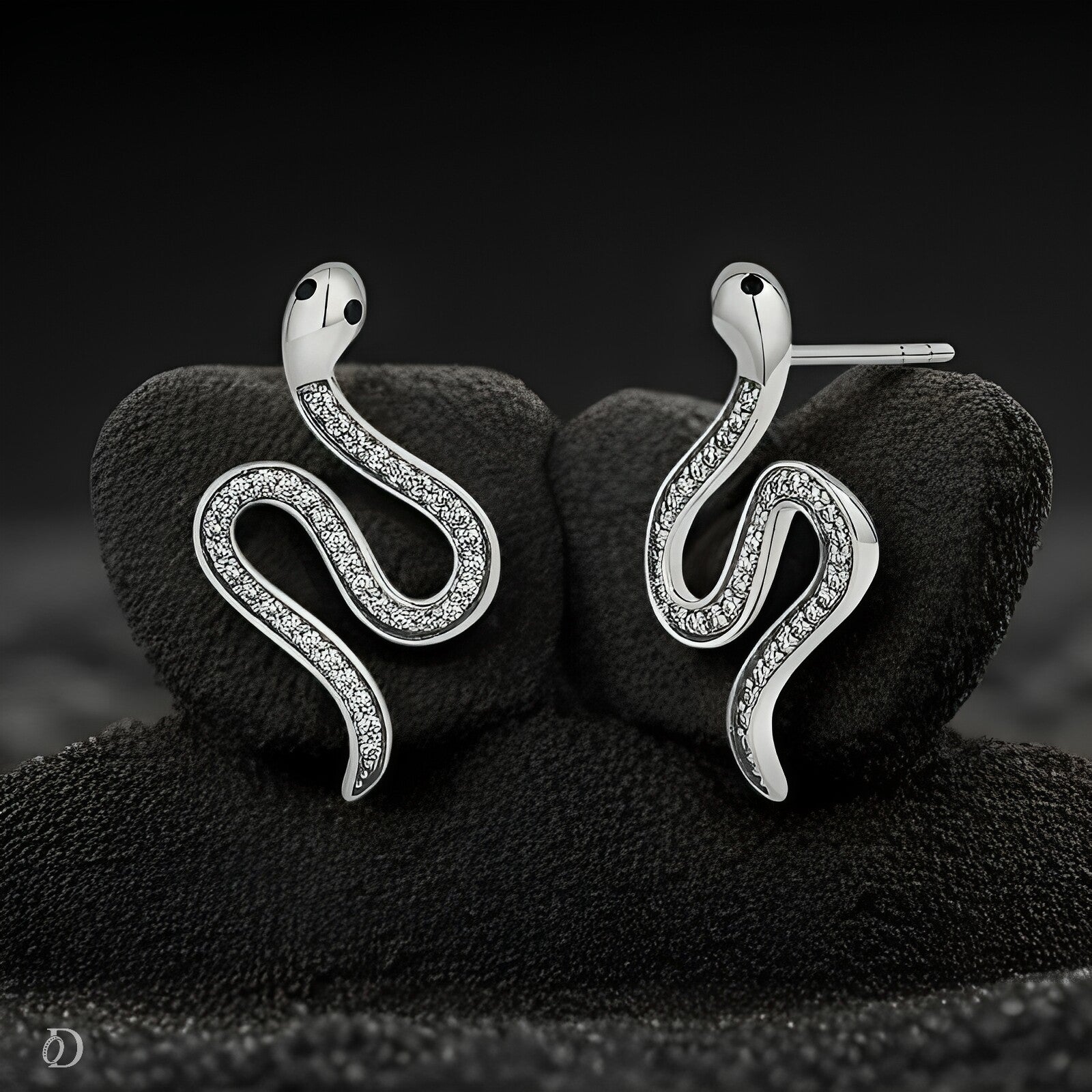 Silver snake-shaped earrings with embedded stones on a black textured surface