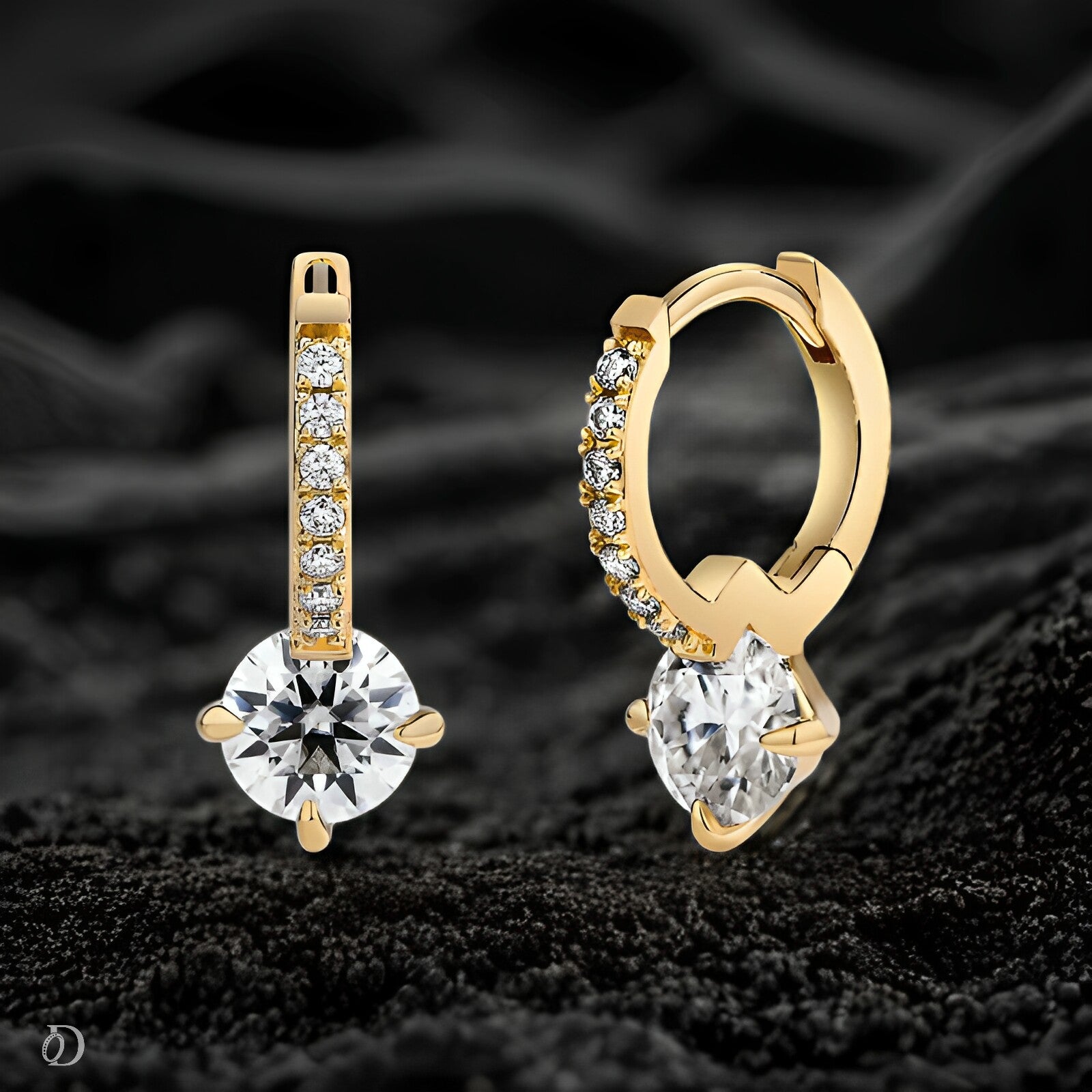 Gold hoop earrings with clear gemstones on a black textured background