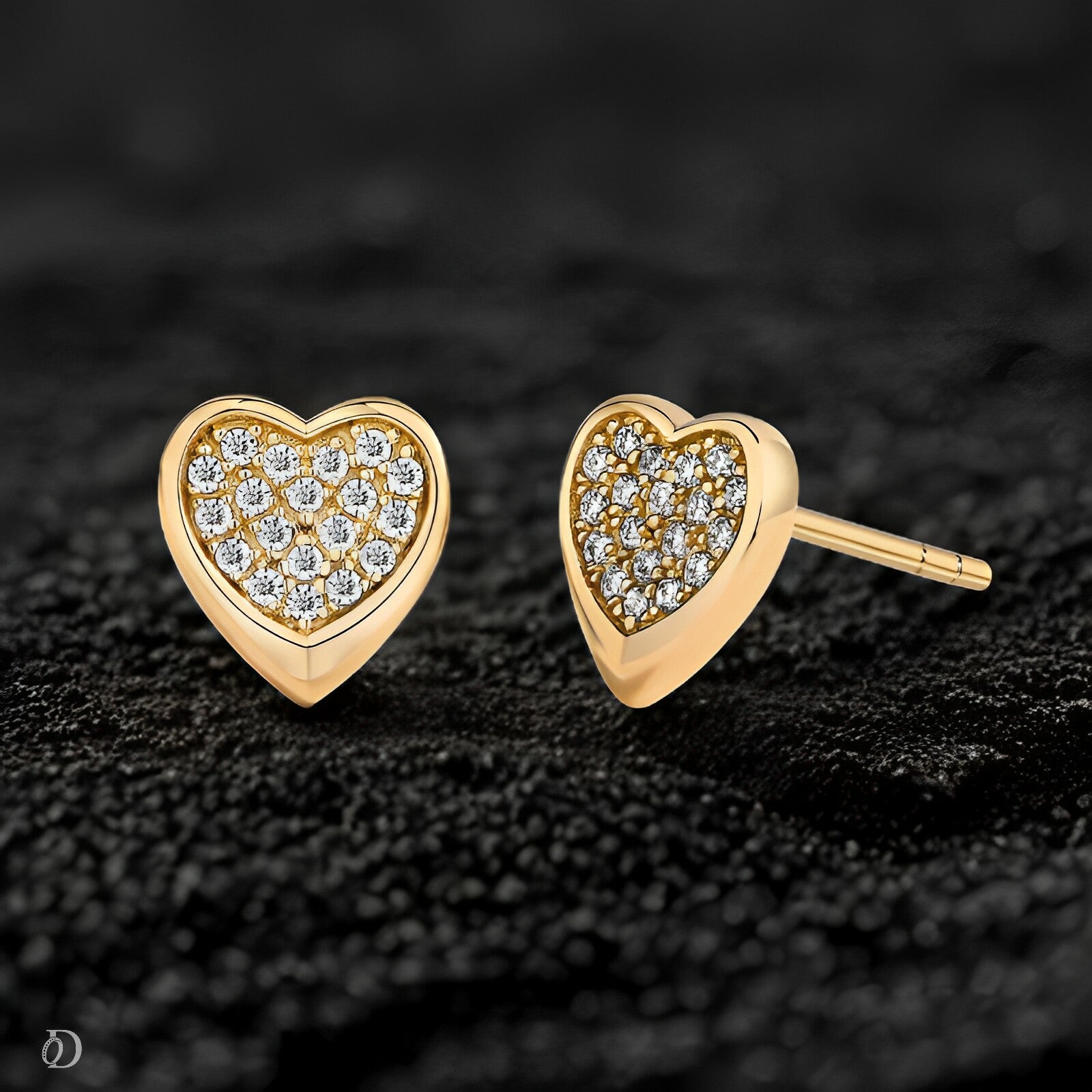 Heart-shaped gold earrings with diamond accents on a dark textured background