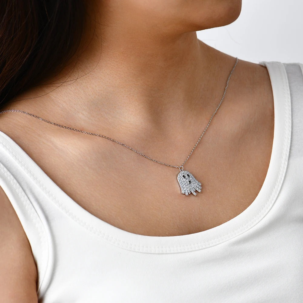 Necklace with a small ghost pendant worn by a person in a white tank top.