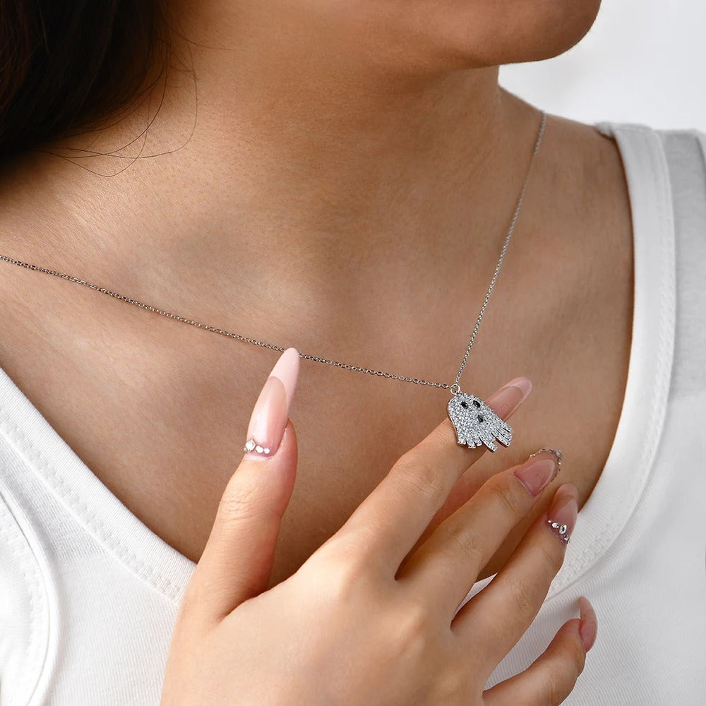 Person wearing a silver necklace with a small ghost pendant, hand touching the necklace.