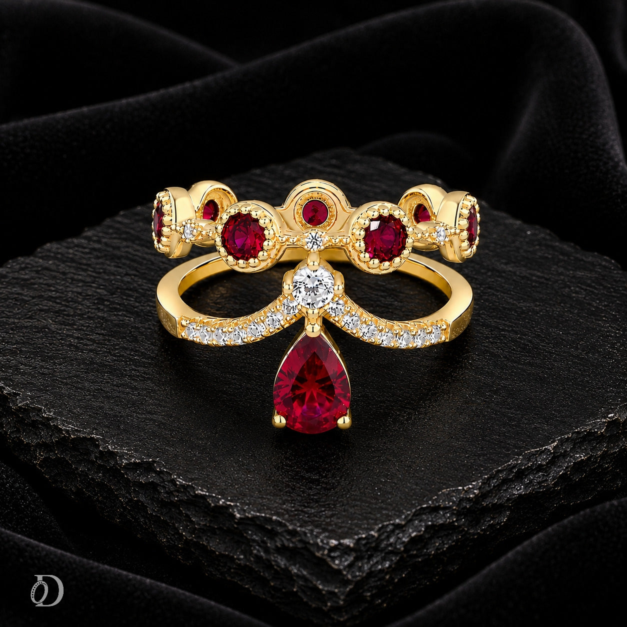 A gold ring with multiple round and teardrop-cut red gemstones and a central clear stone, displayed on a textured black surface with draped black fabric in the background.