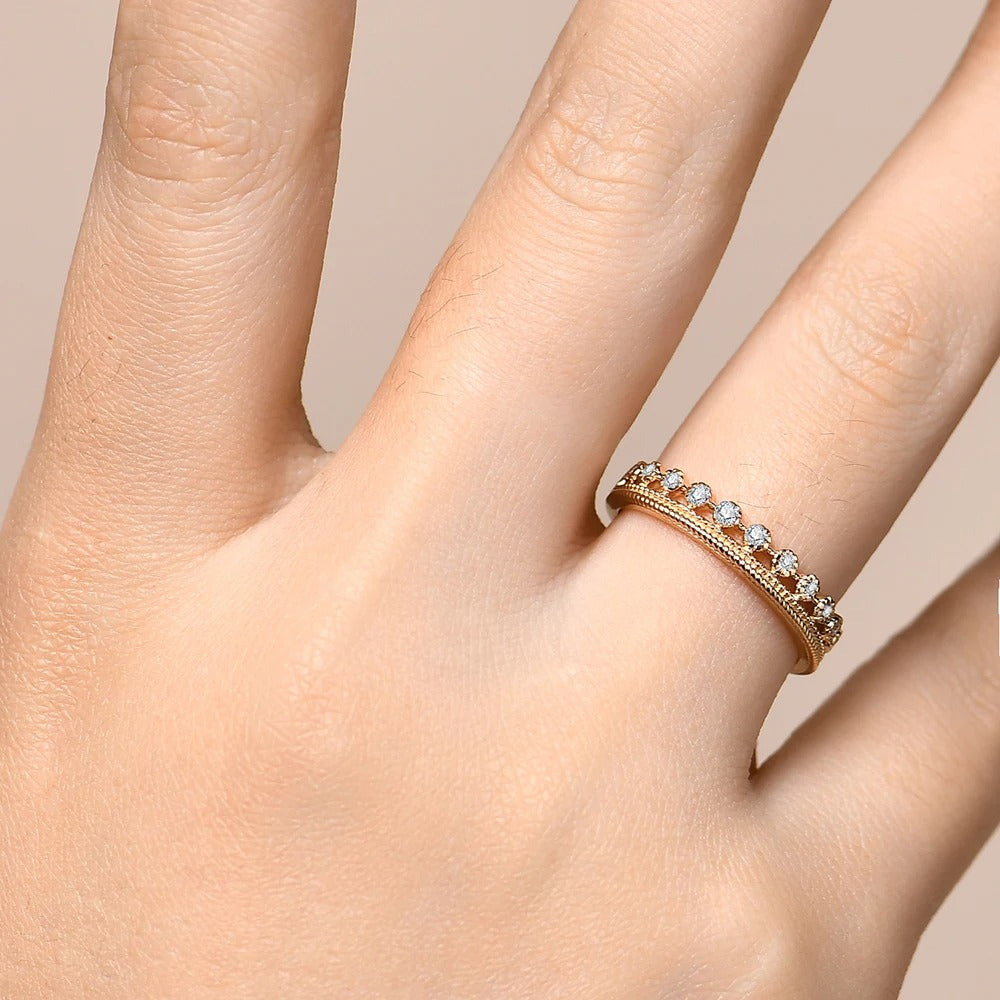 Rose gold ring with small stones on a hand against a beige background
