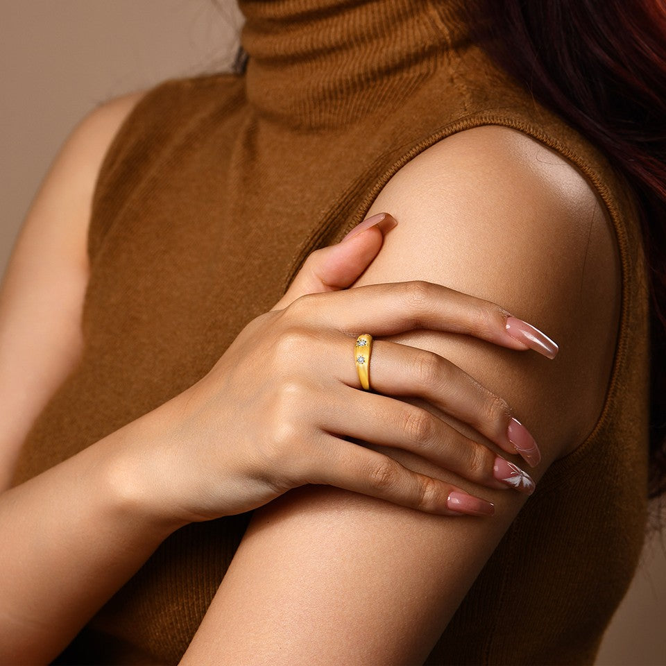 Close-up of a person wearing a gold ring with small stones on a neutral background