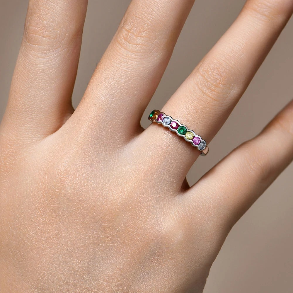 Close-up of a hand wearing a ring with colorful gemstones on a neutral background