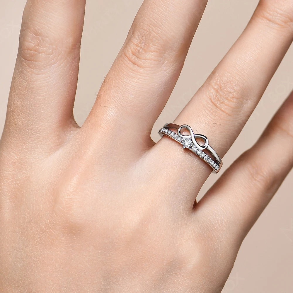 Hand wearing a silver ring with an infinity symbol on a beige background