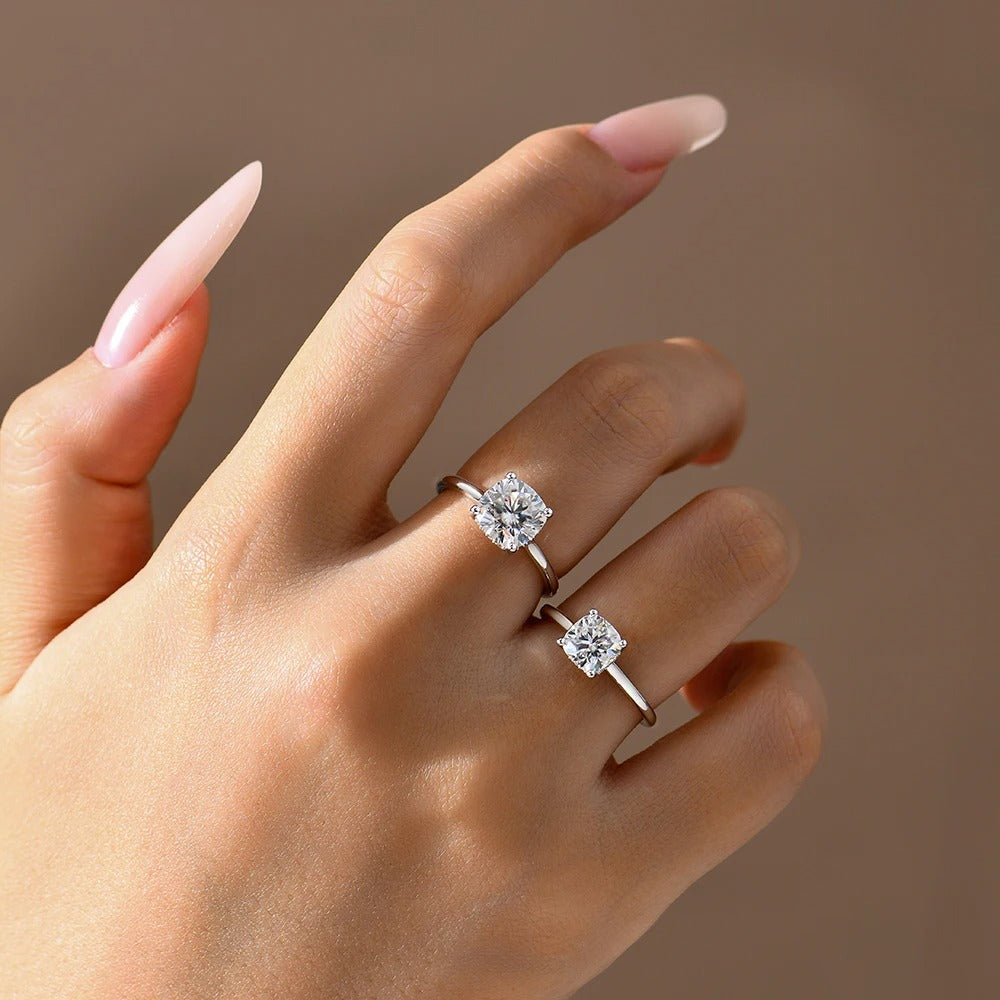 Hand wearing two diamond rings on a neutral background