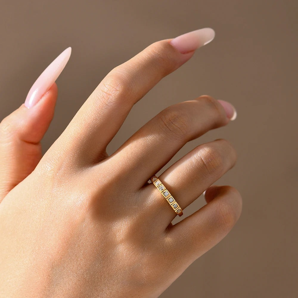 Hand wearing a gold ring with small diamonds on a beige background
