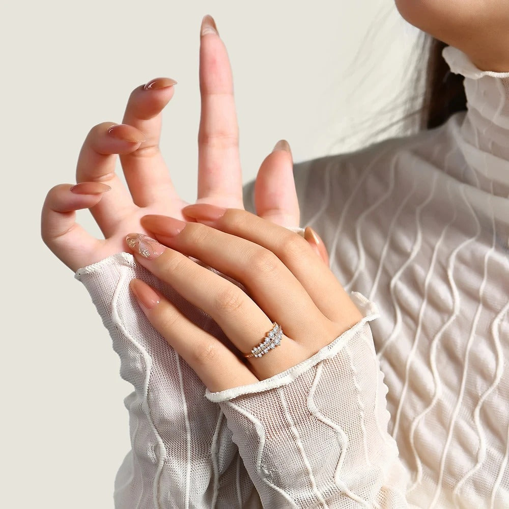 Close-up of a hand with a ring, wearing a white textured sleeve against a neutral background