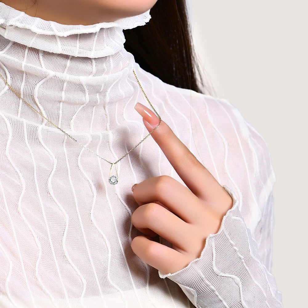 Person wearing a delicate necklace with a small pendant, pointing to it.