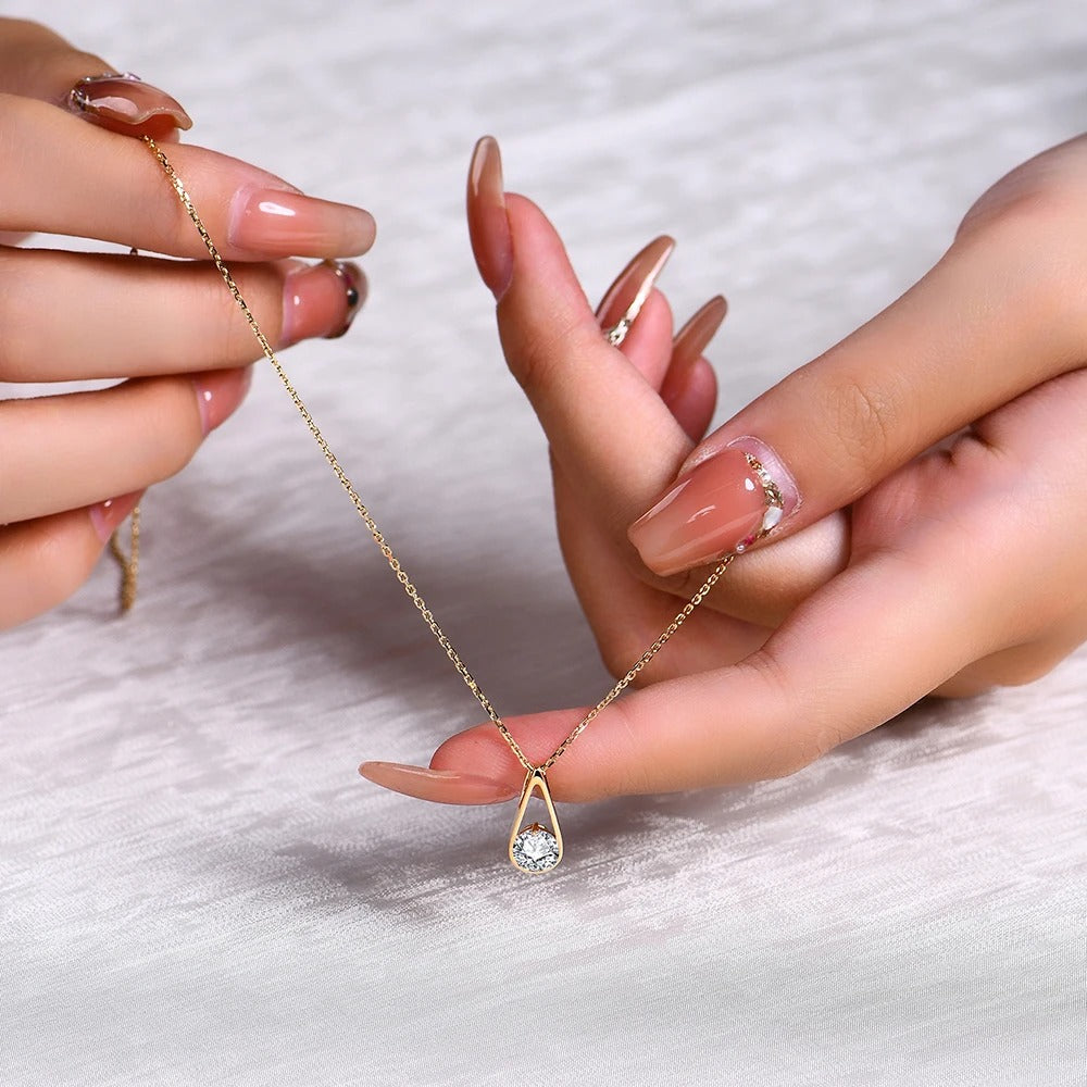 Gold necklace with a teardrop-shaped pendant held by two hands against a light background