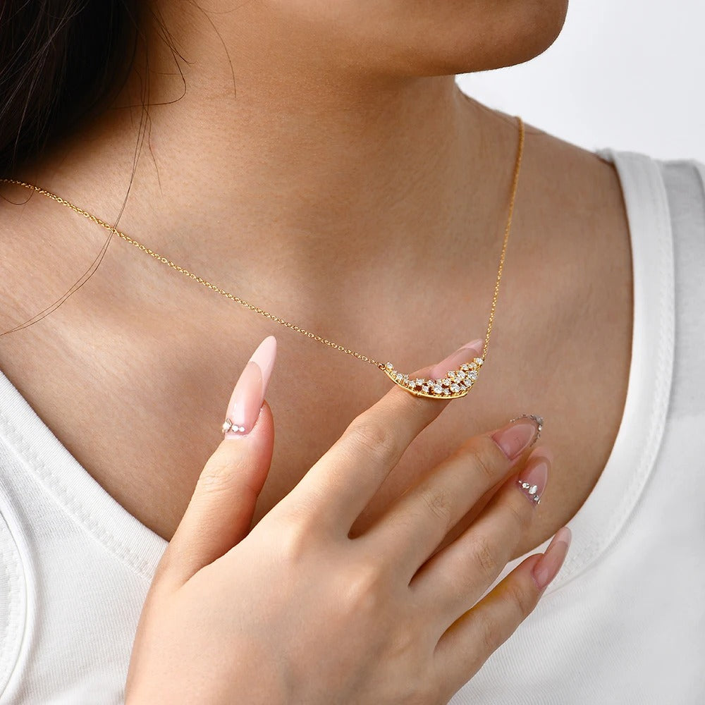 Gold necklace with a crescent moon design worn by a person, with a close-up of the necklace and hand.