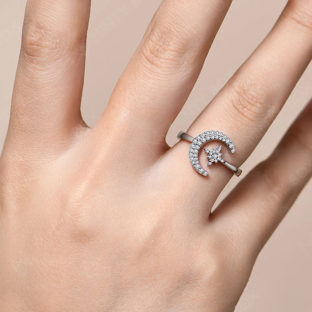 Silver ring with a moon and star design on a hand against a beige background