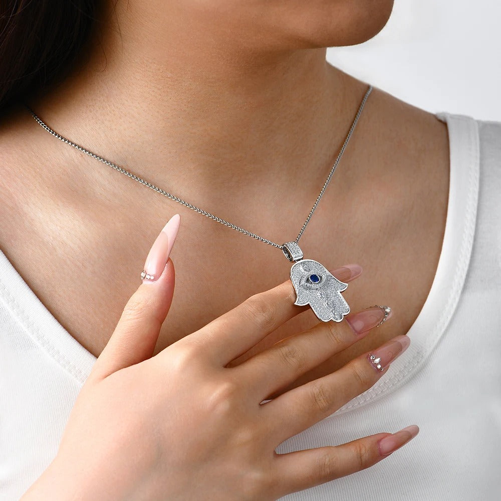 Silver Hamsa hand necklace with blue stone worn by a person on a white background