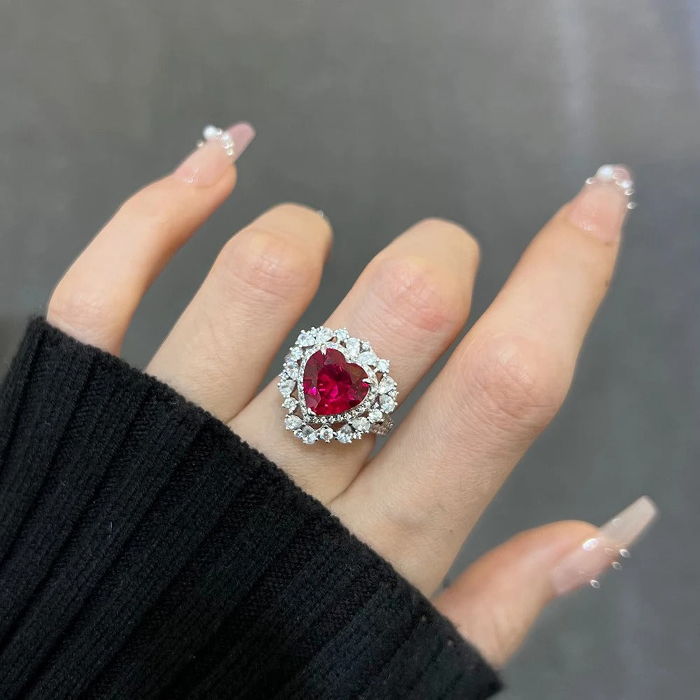 Heart-shaped gemstone ring on a hand with a black sleeve against a dark background