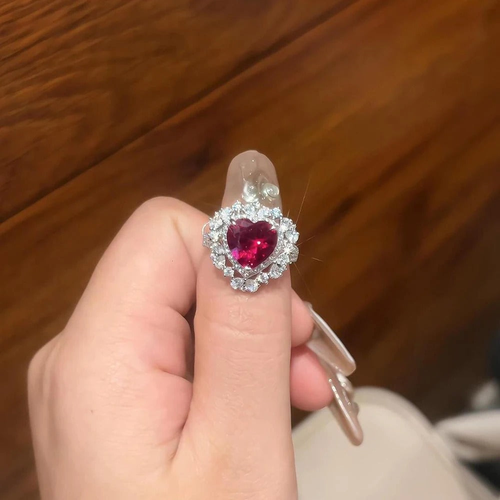 Heart-shaped gemstone ring held by a hand against a wooden background
