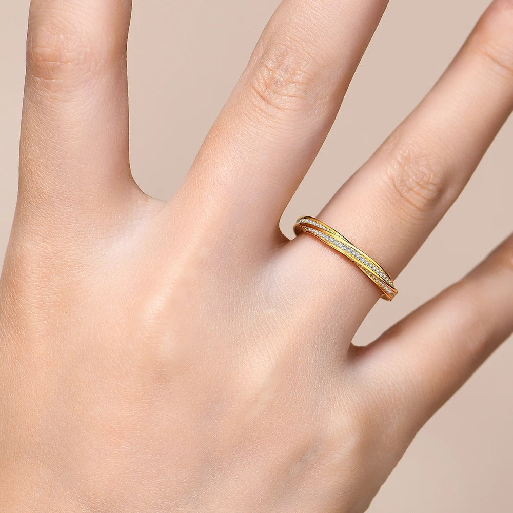 Gold ring with small stones on a person's finger against a beige background