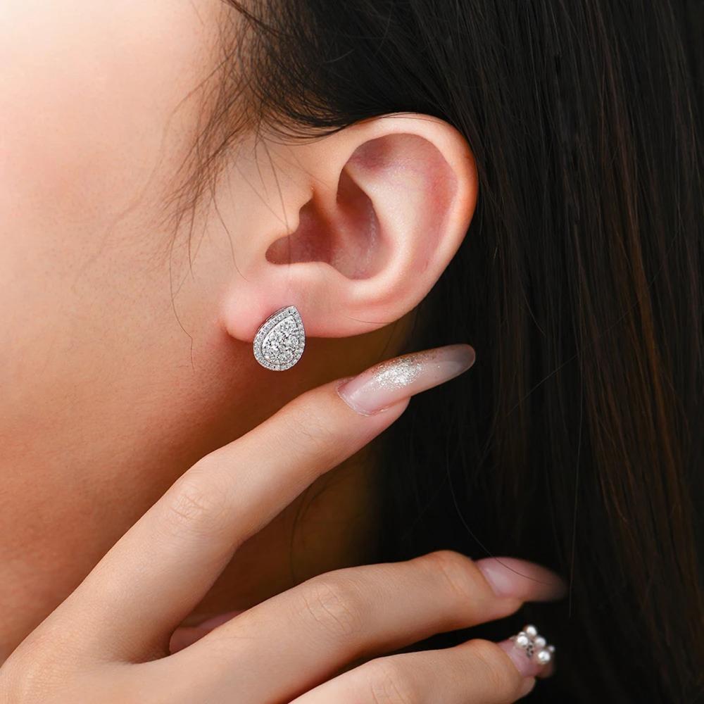 Close-up of a person wearing a silver teardrop earring with a hand touching the ear.