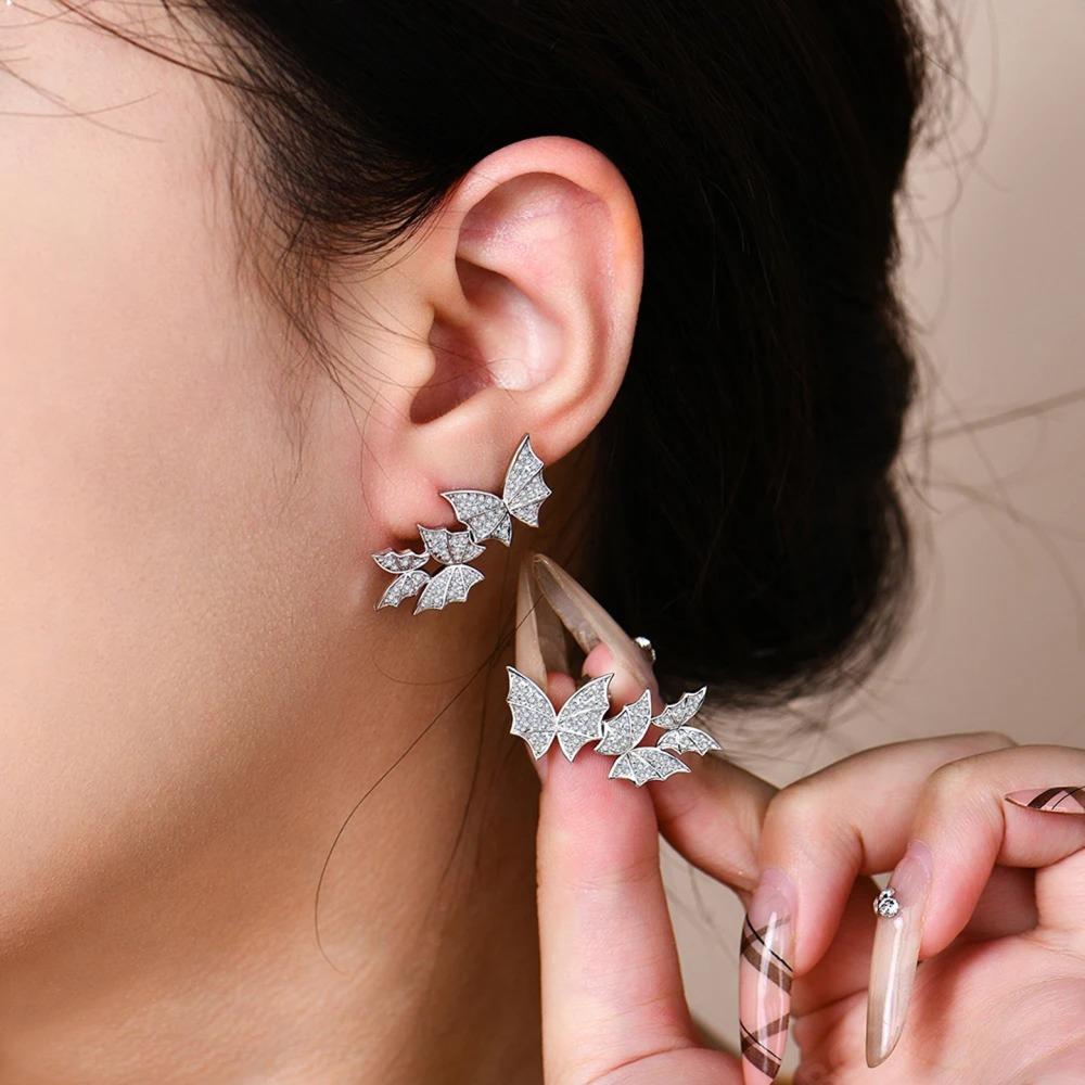 Close-up of a person wearing butterfly-shaped earrings with a neutral background