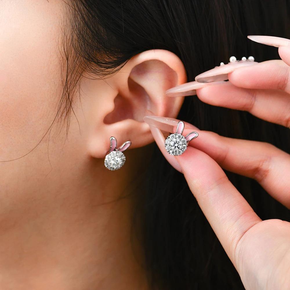 Person wearing a silver earring with bunny ears and holding another similar earring.