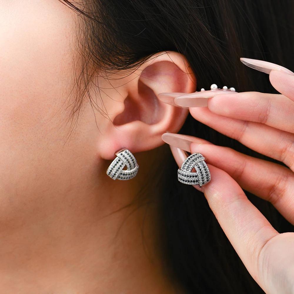 Person wearing silver earrings with a close-up of an ear and hand holding a small round object.