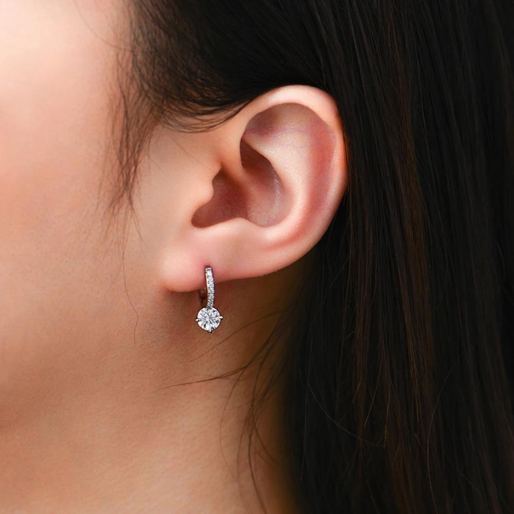 Close-up of an ear wearing a diamond earring with dark hair and skin background