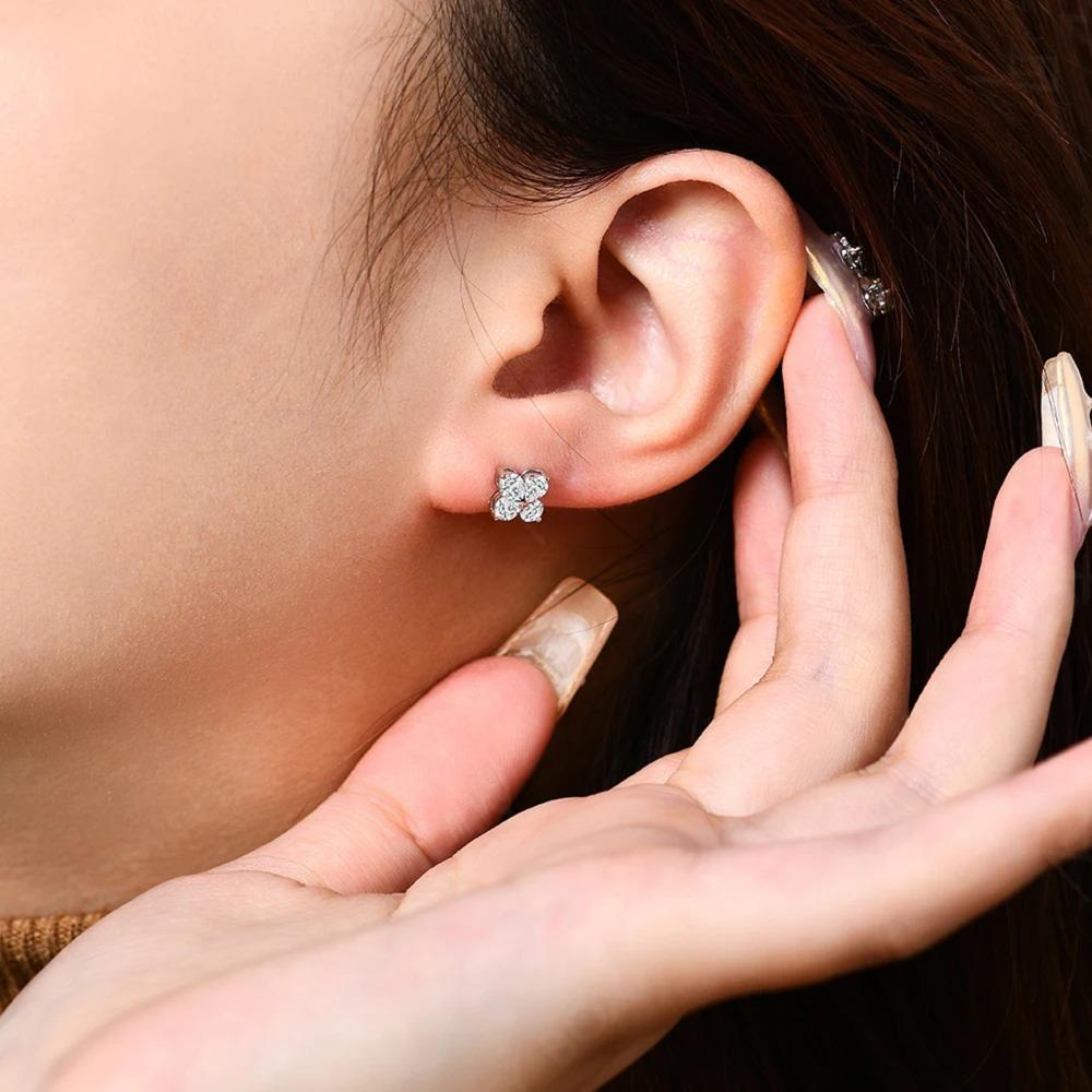 Close-up of an ear with diamond stud earrings and a hand holding the ear.