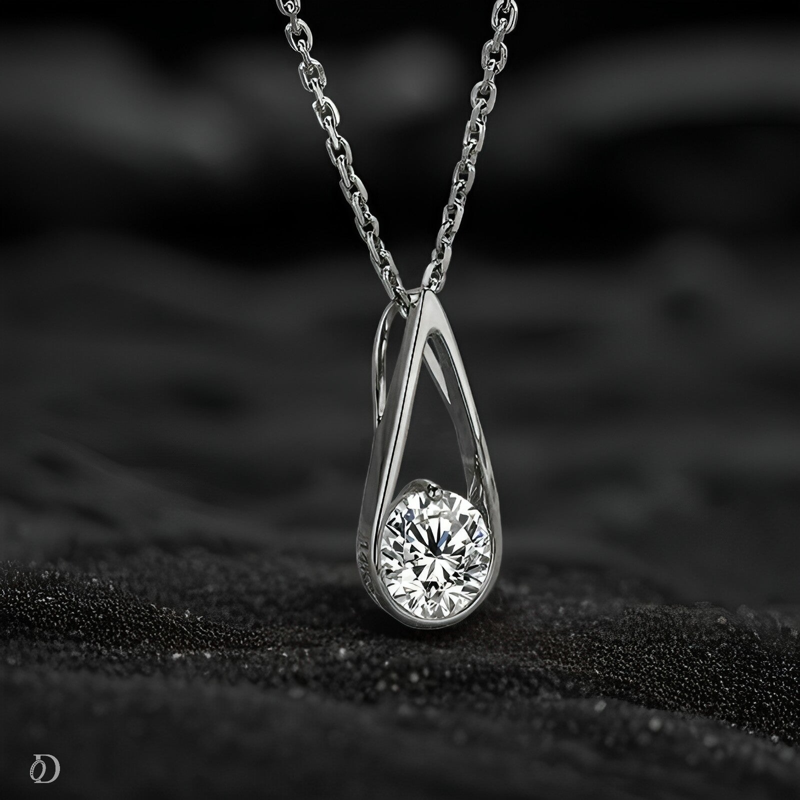 Silver teardrop-shaped pendant with a diamond on a black textured surface