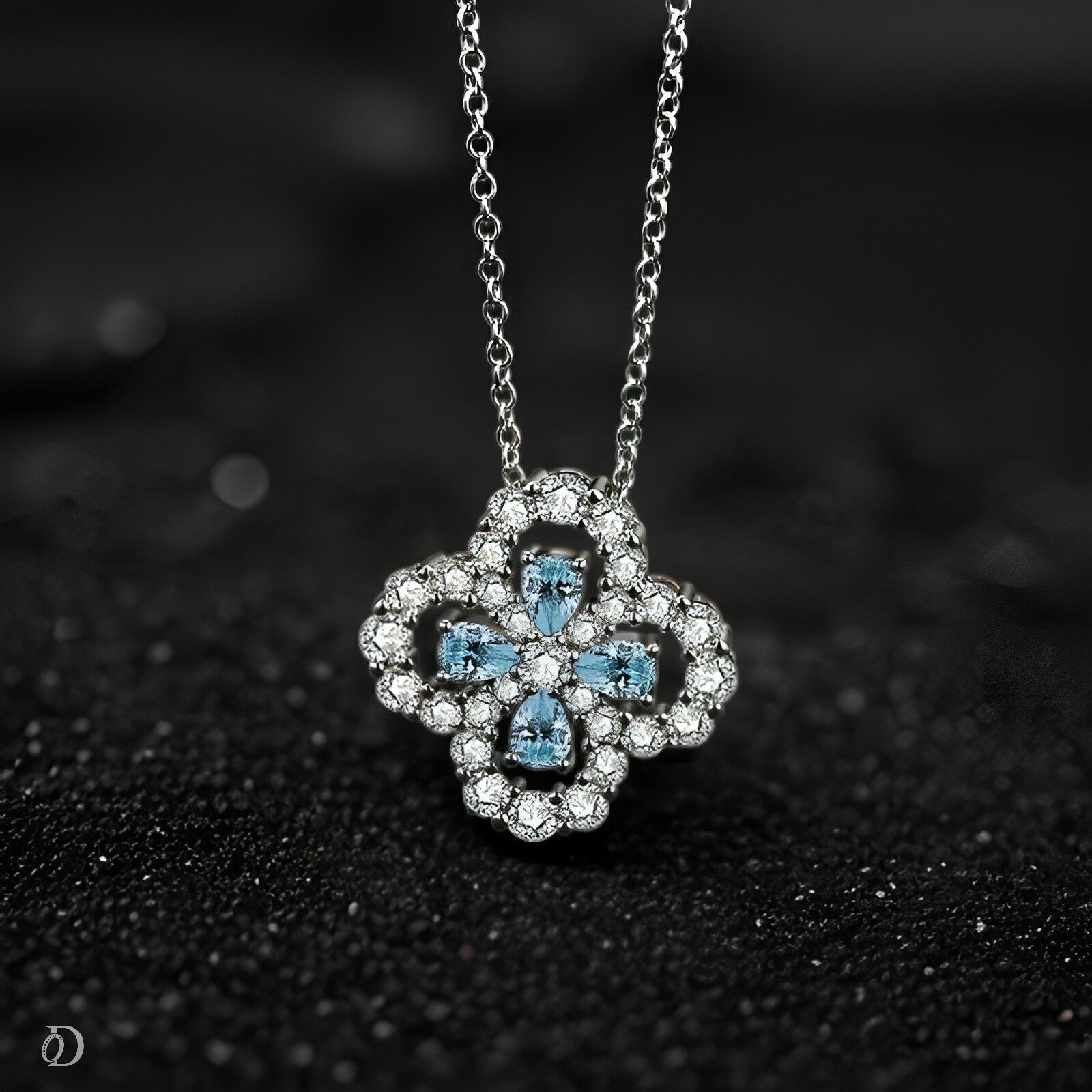 Silver necklace with a decorative pendant featuring blue stones on a black textured background