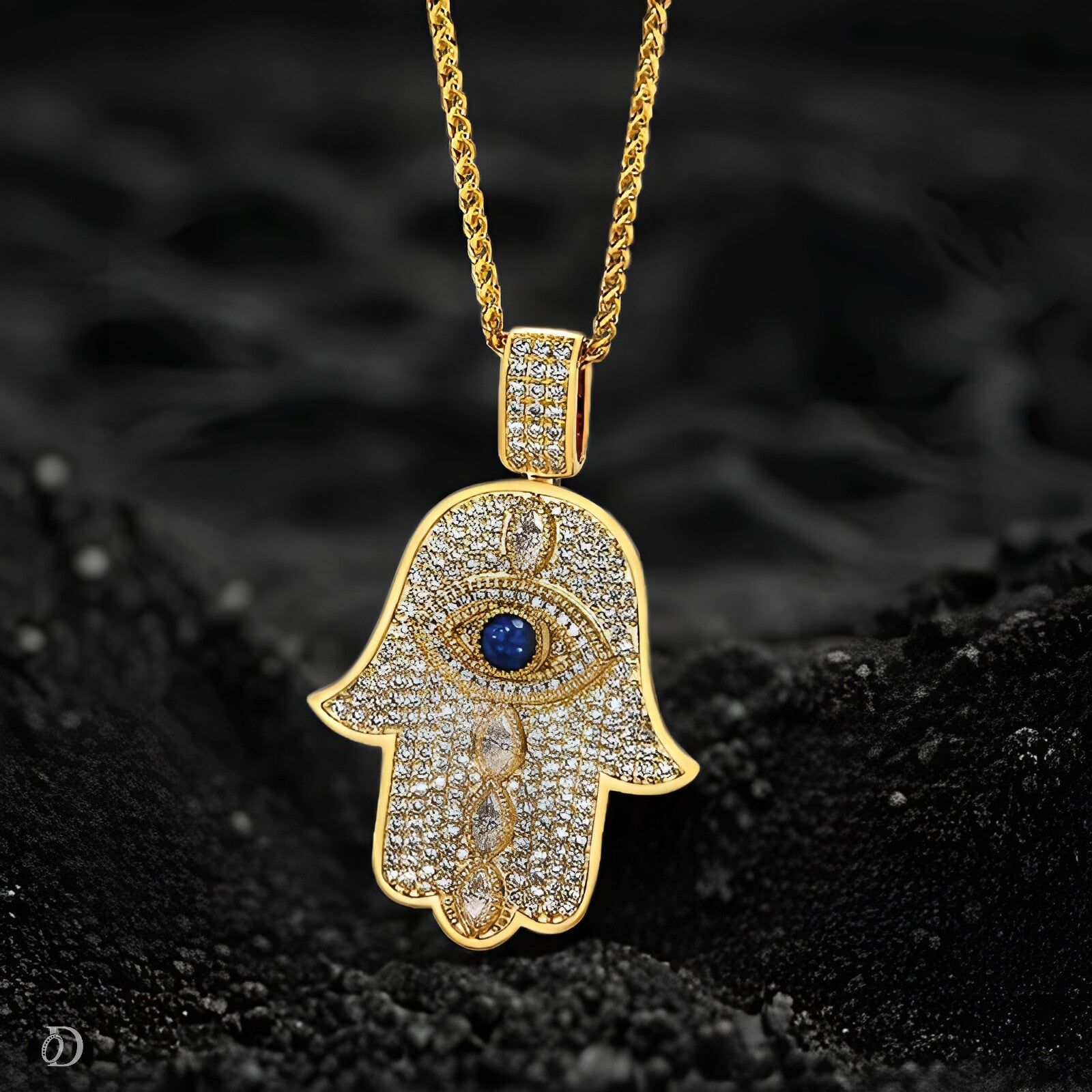 Gold Hamsa hand pendant with a blue stone on a black textured background