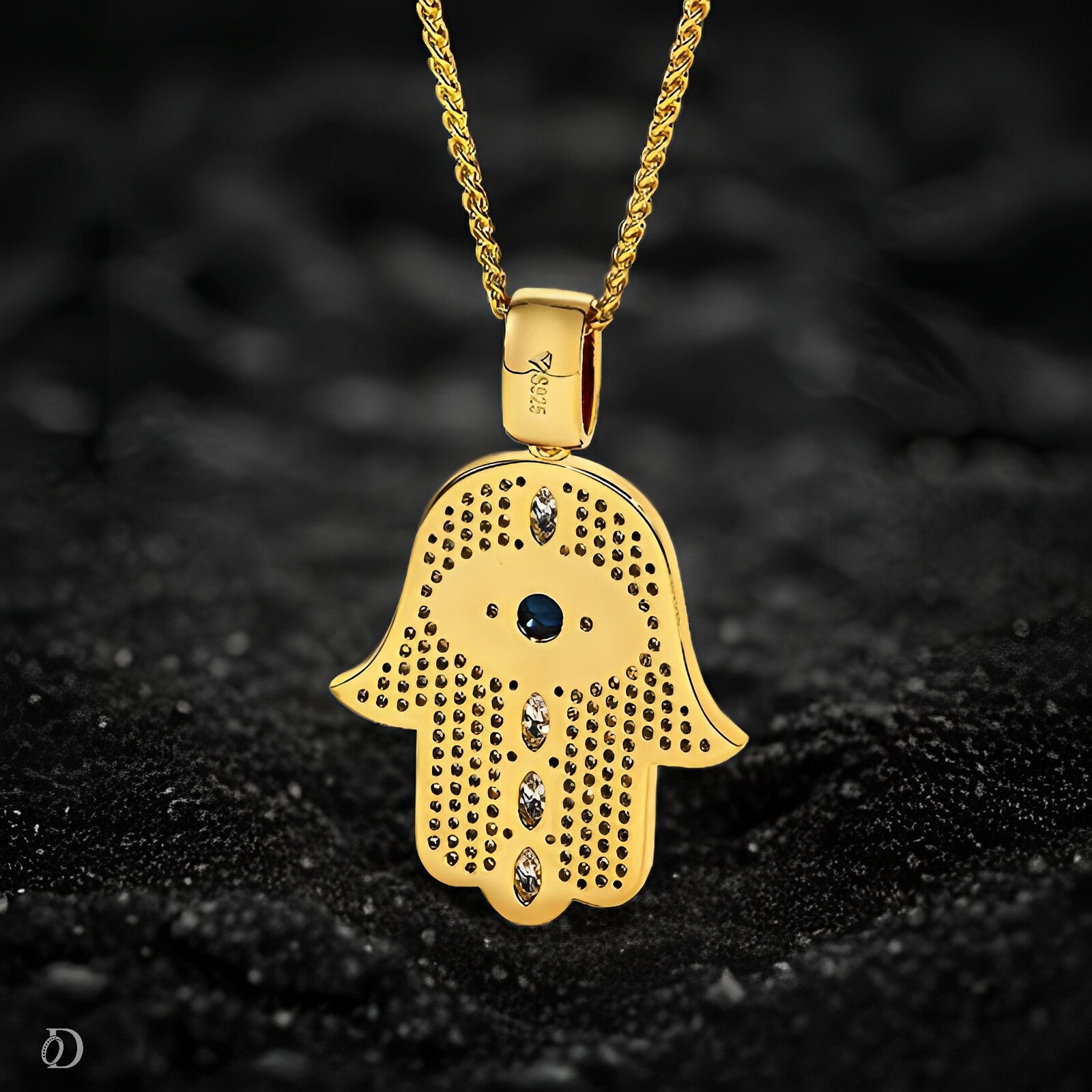 Gold Hamsa pendant with embedded stones on a dark textured background