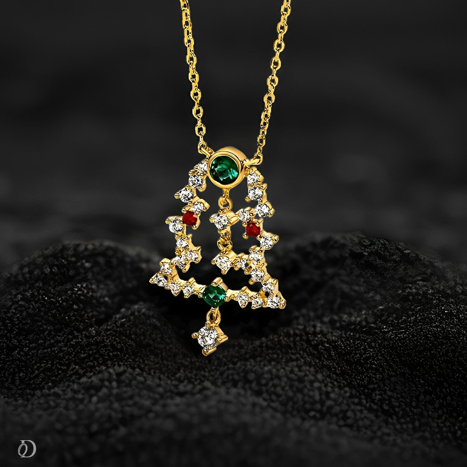 Gold Christmas tree pendant with green and red gemstones on a dark background