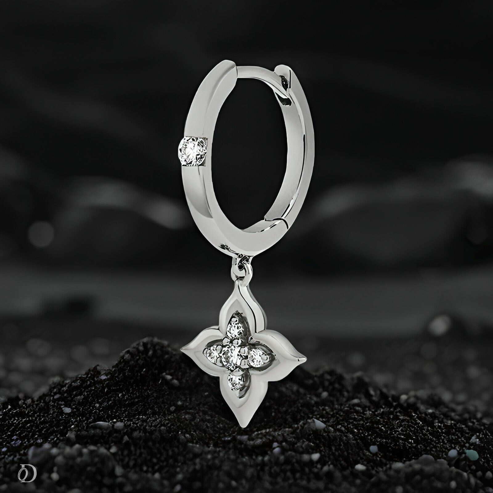 Silver hoop earring with a floral pendant on a dark background