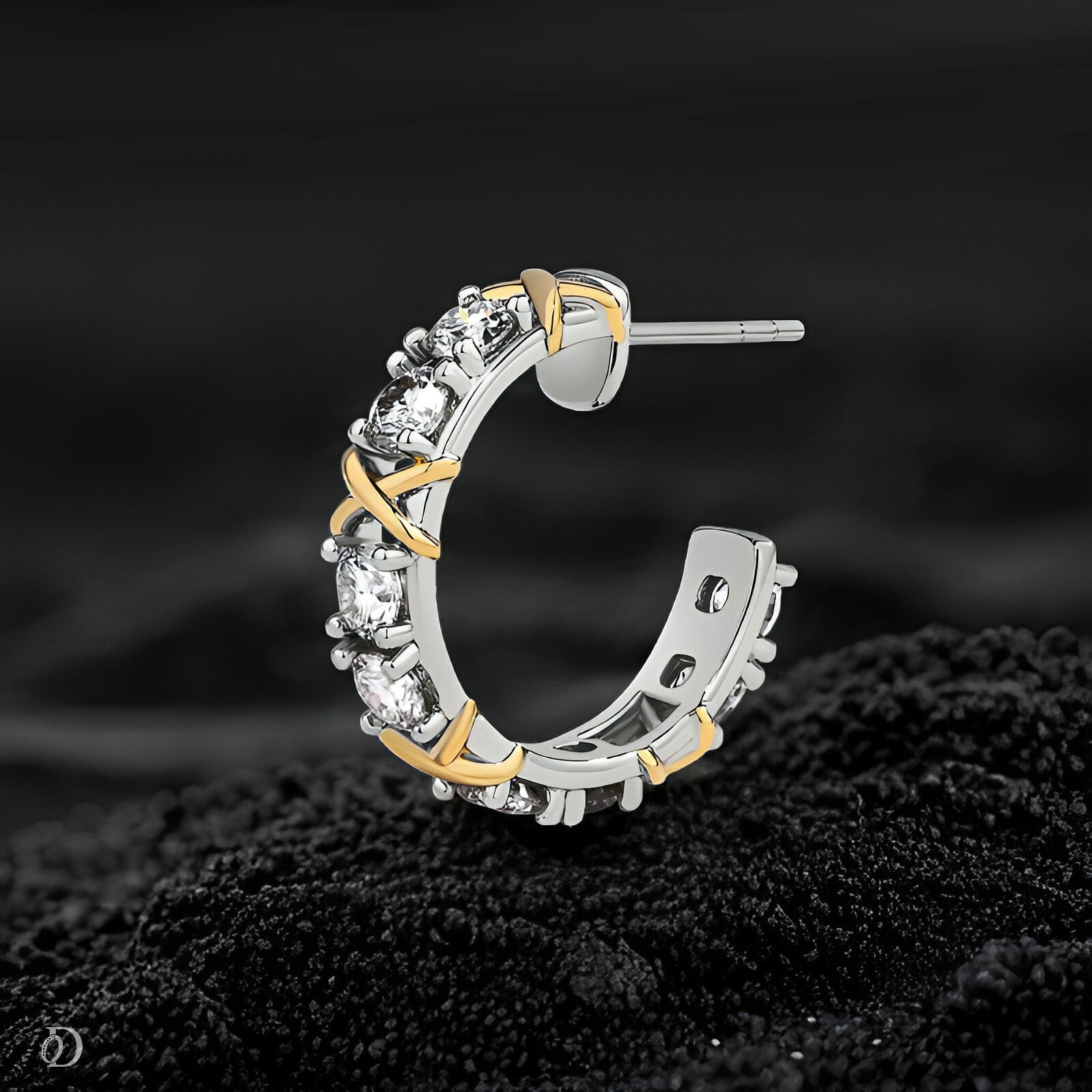 Silver and gold hoop earring with clear stones on a dark textured surface