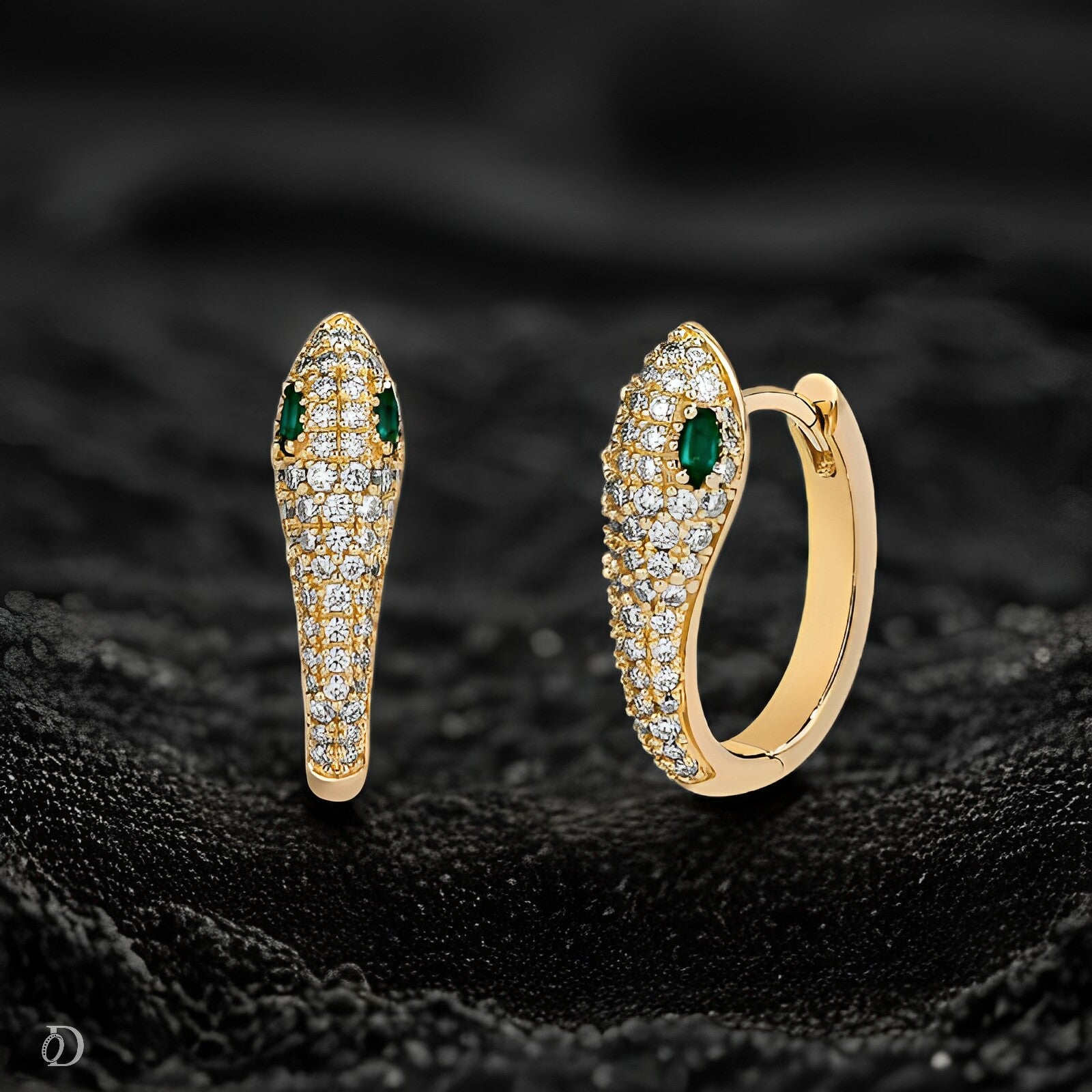 Gold snake-shaped earrings with green gemstones on a black textured background