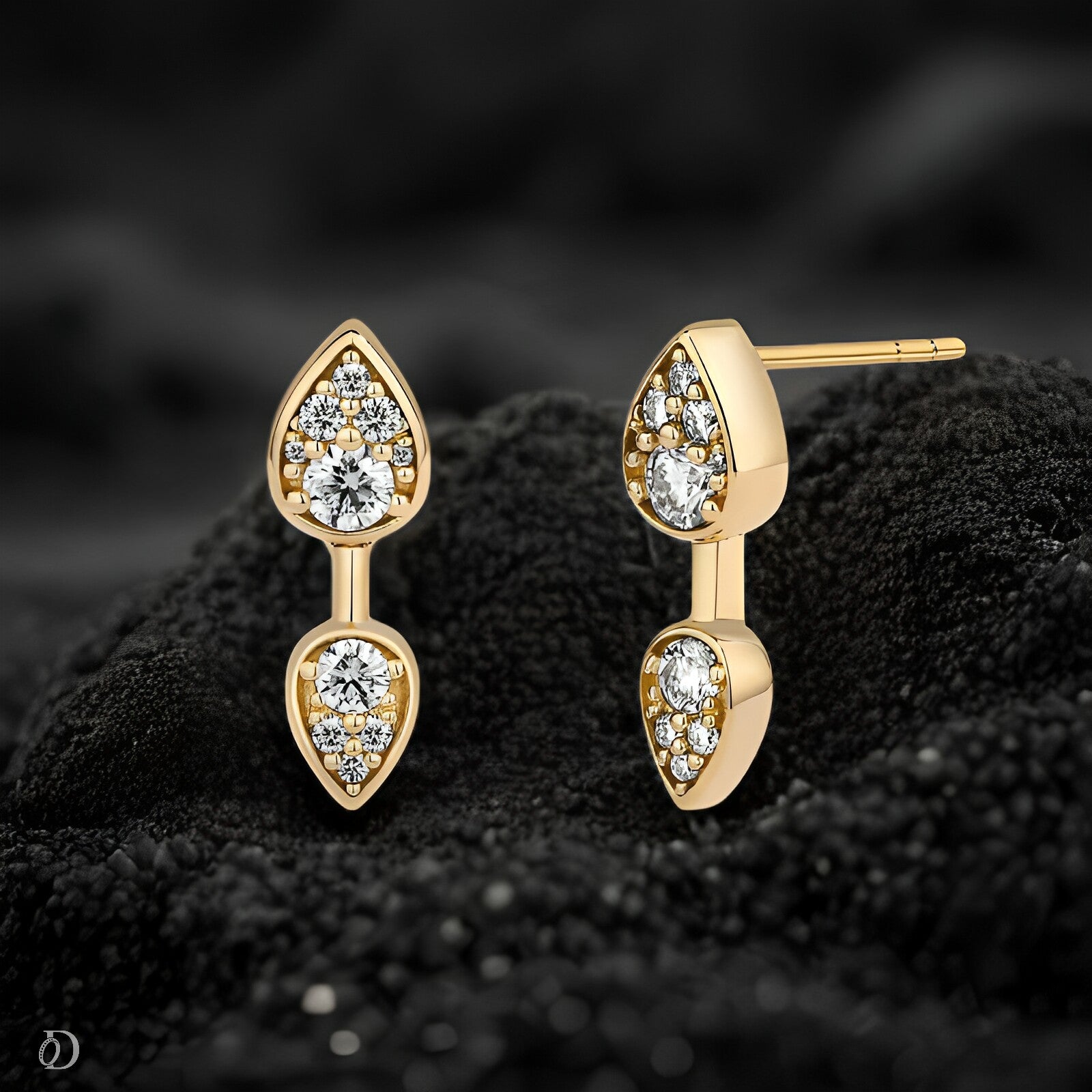 Gold earrings with clear gemstones on a textured black surface