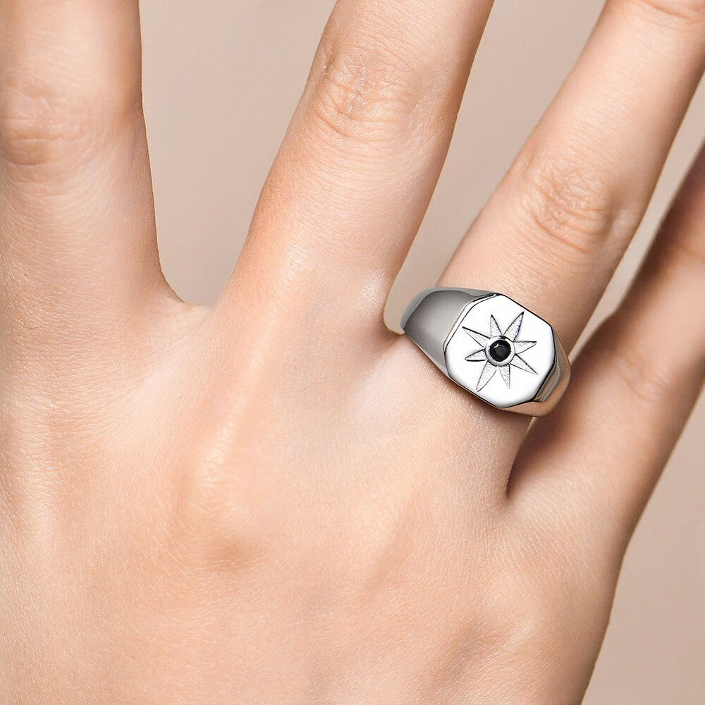 Silver ring with star design on a person's finger against a beige background