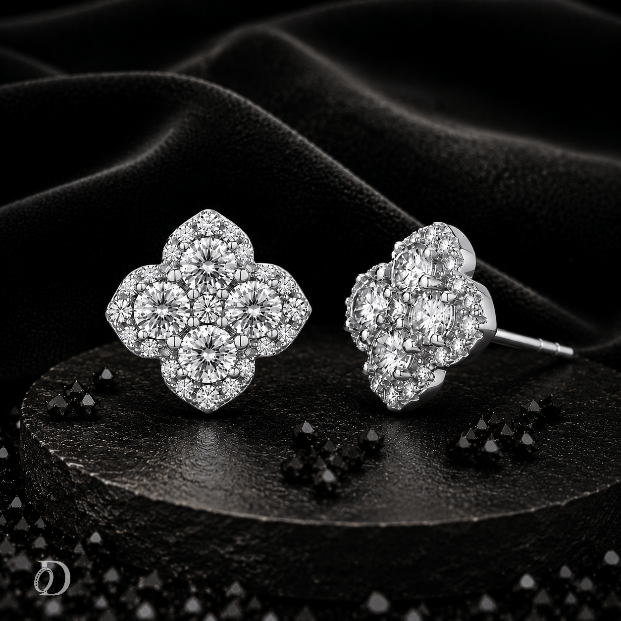 A pair of silver-toned cluster stud earrings with clear gemstones, arranged on a dark textured surface with draped black fabric in the background.