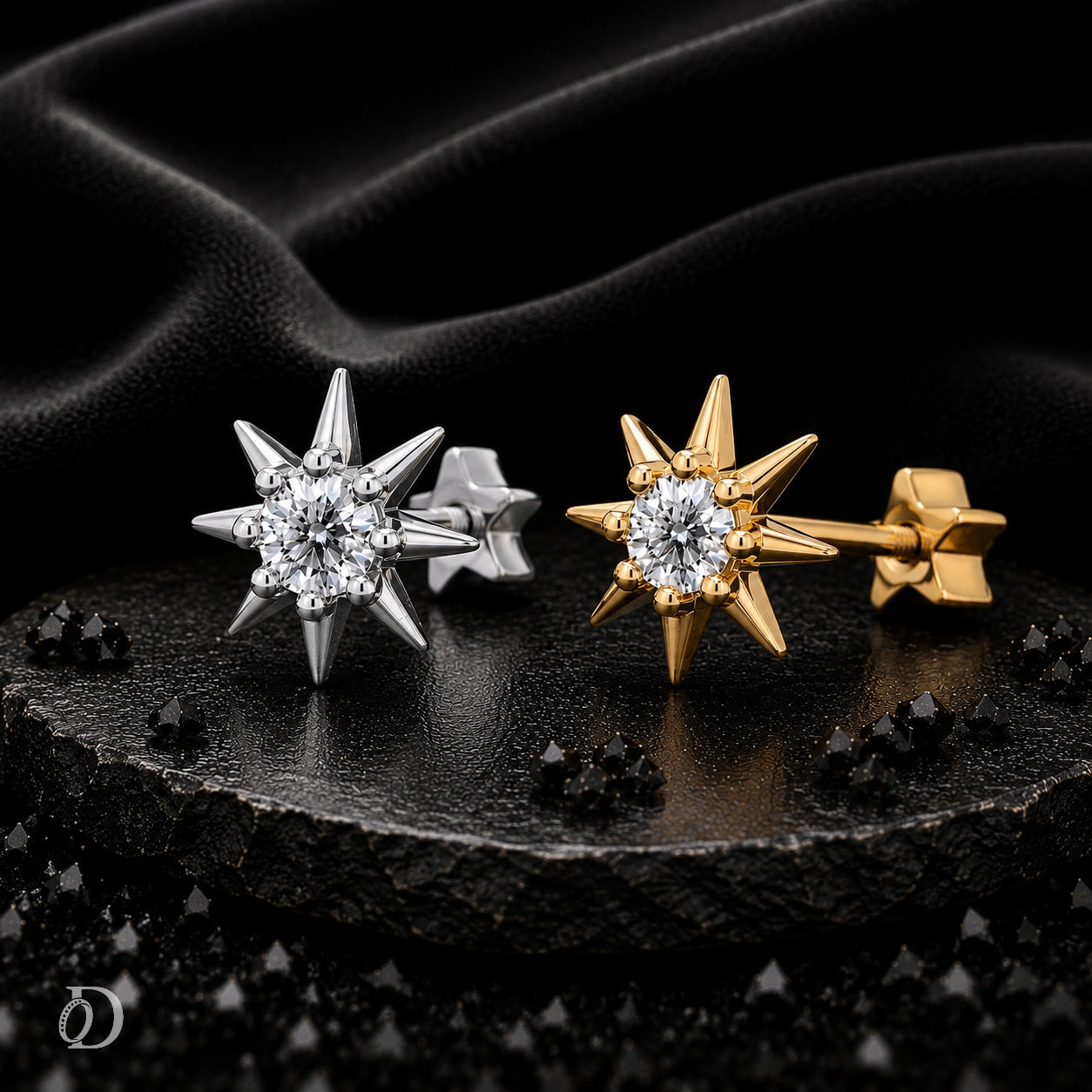Two star-shaped stud earrings displayed on a dark textured surface with draped black fabric behind them. One earring is silver-toned and the other is gold-toned, both featuring clear gemstone centers.