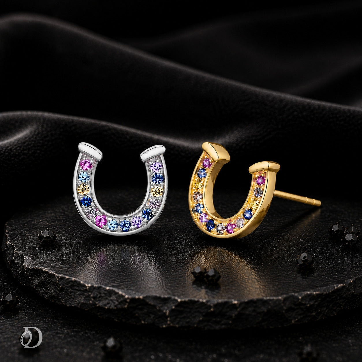 Two horseshoe-shaped stud earrings displayed on a dark textured surface. One earring is silver-toned with multicolored gemstones, and the other is gold-toned with multicolored gemstones.