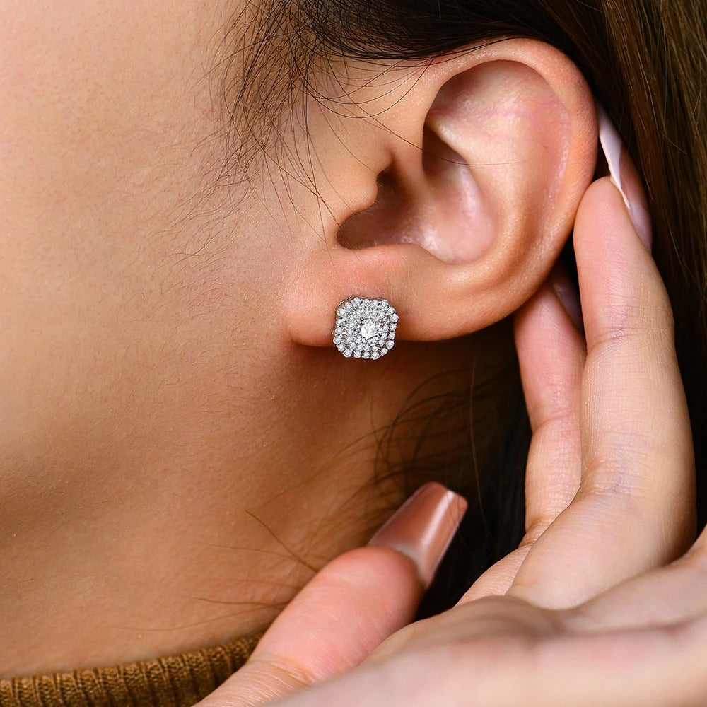 Close-up of an ear wearing a diamond stud earring with a hand adjusting it.