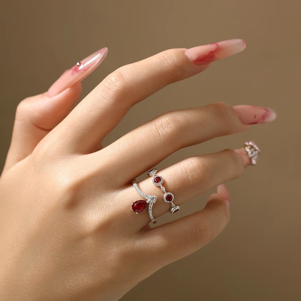 Hand wearing a silver ring with red gemstones on a neutral background