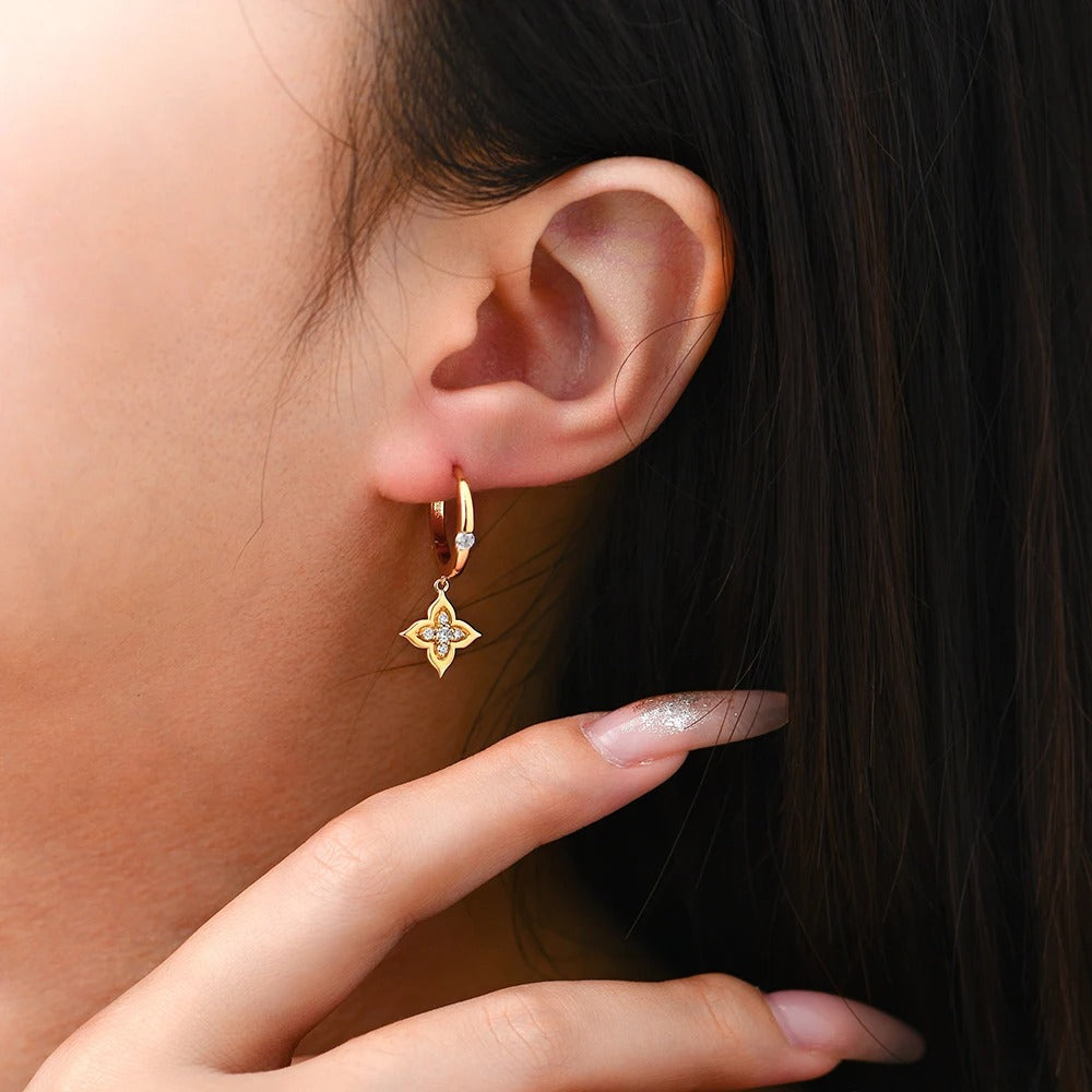 Close-up of a person wearing a gold earring with a diamond, held by a hand.