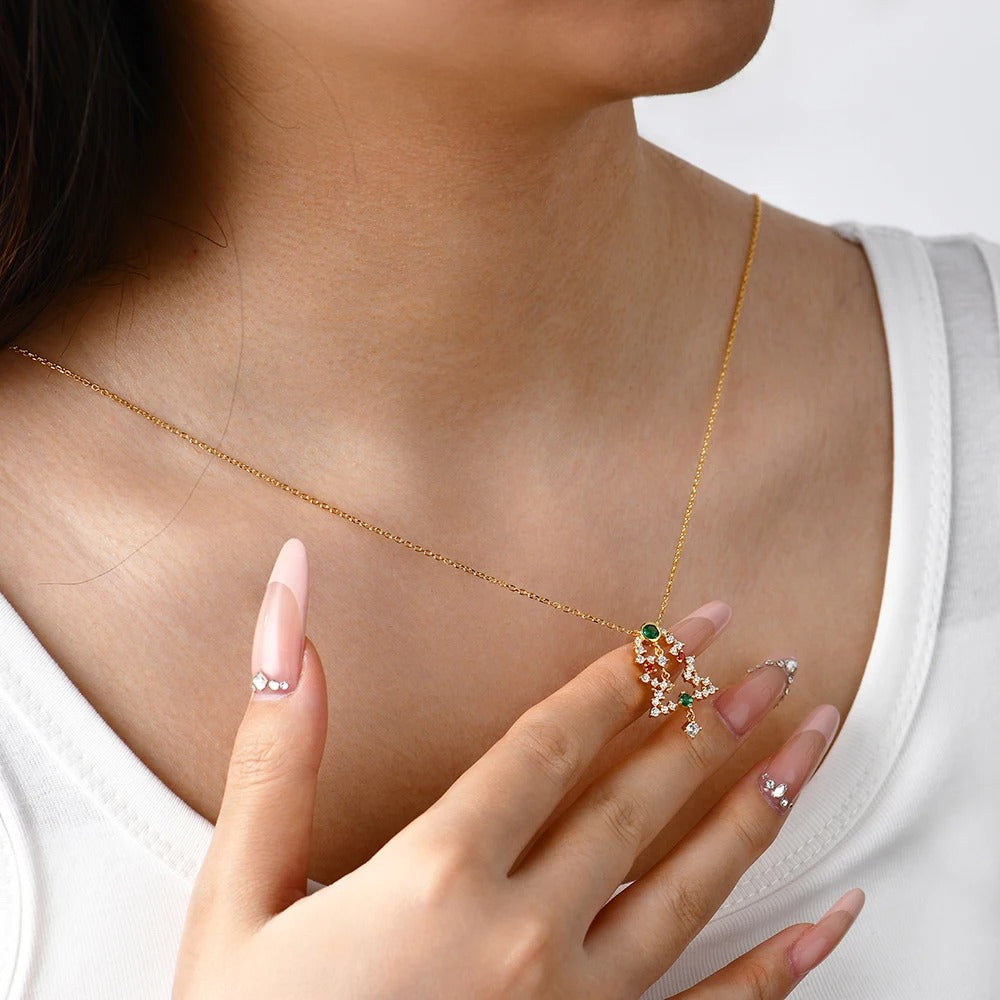 Gold necklace with a green gemstone pendant worn by a person, with a hand holding a matching ring.