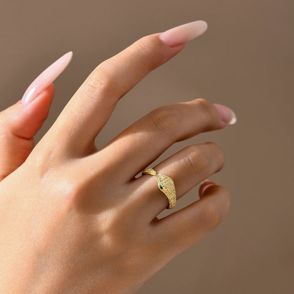 Gold snake-shaped ring on a hand with a neutral background