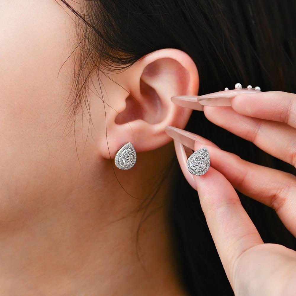 Teardrop-shaped earrings being worn and held by a hand