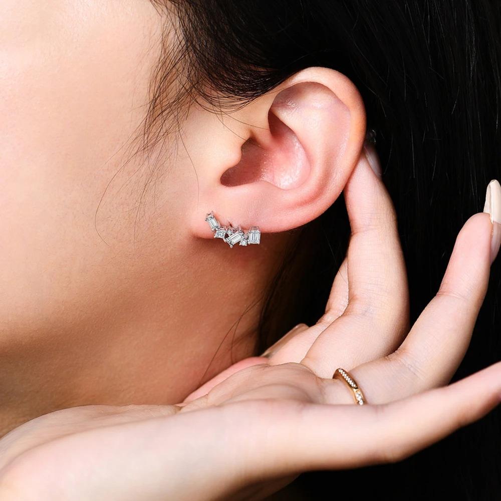 Close-up of an ear wearing a diamond earring with a hand holding a ring.